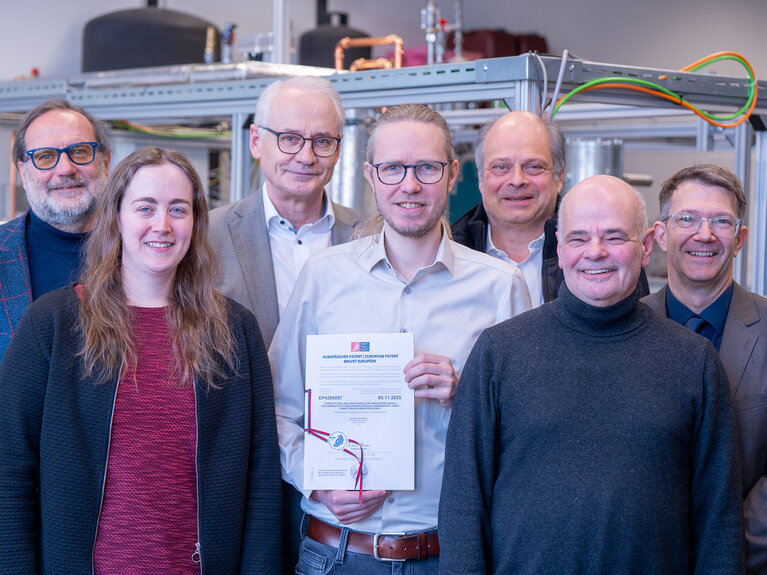 Sechs Männer und eine Frau stehen zusammen. Der Herr in der Mitte hält die Bescheinigung über das Zertifikat in der Hand.