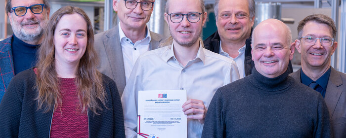 Sechs Männer und eine Frau stehen zusammen. Der Herr in der Mitte hält die Bescheinigung über das Zertifikat in der Hand.