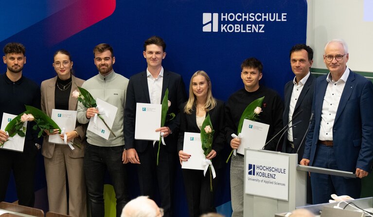 Sechs Männer und zwei Frauen stehen mit ihren Auszeichnungen und Blumen vor dem Banner der Hochschule Koblenz