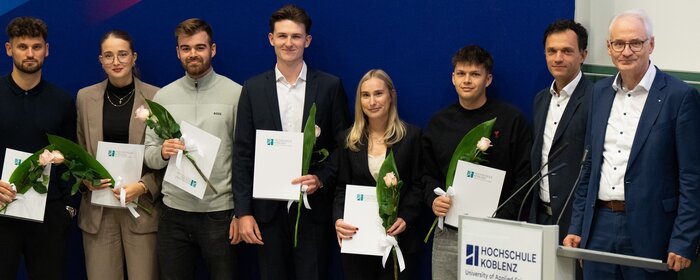 Sechs Männer und zwei Frauen stehen mit ihren Auszeichnungen und Blumen vor dem Banner der Hochschule Koblenz