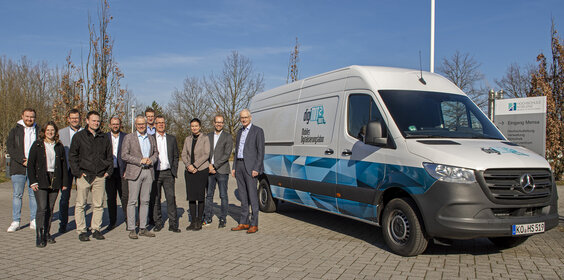Ein Gruppe von Personen steht vor einem Transporter.