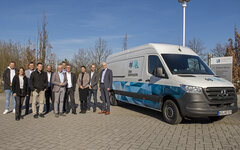 Ein Gruppe von Personen steht vor einem Transporter.