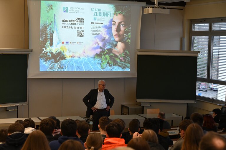 Der Präsident der Hochschule steht vorne vor dem Begrüßungsplakat im Vorlesungsraum.