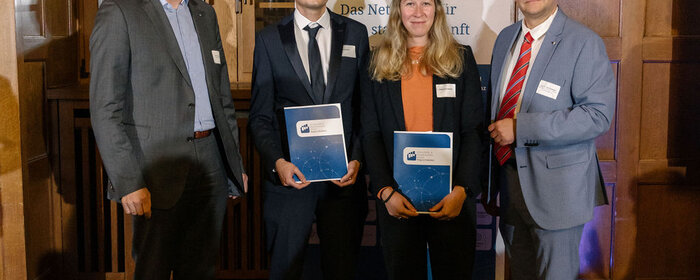 Vier Personen, davon eine Frau und zwei Männer stehen zur Preisverleihung zusammen.