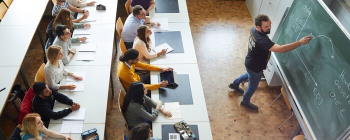 Studierende im Seminarraum. Ein Dozent steht an der Tafel.