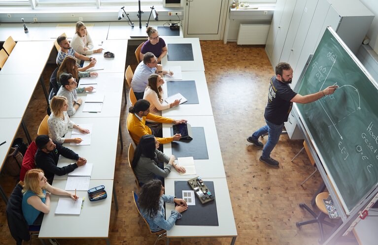 Studierende im Seminarraum. Ein Dozent steht an der Tafel.