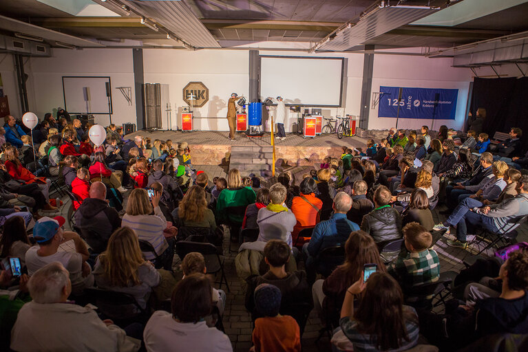 Eine teilnehmende Großgruppe von hinten mit Blick auf die Bühne, wo im Rahmen der Nacht der Technik Experimente vorgeführt werden.