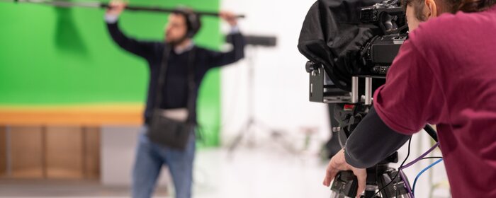 Fernsehstudio mit einer Dame an der Kamera und einem Herrn, der ein Mikrophon hält. 