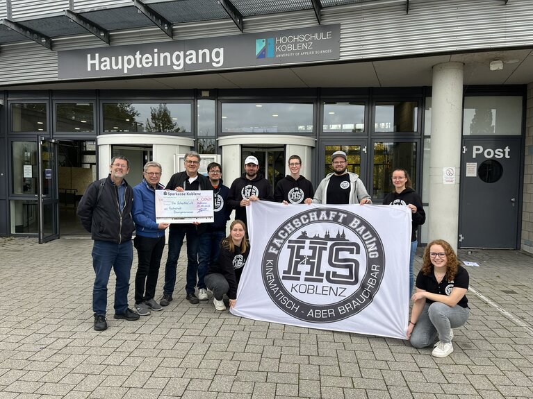 Studierende und Vereinsmitarbeitende mit dem Scheck zur Spendenübergabe vor der Hochschule