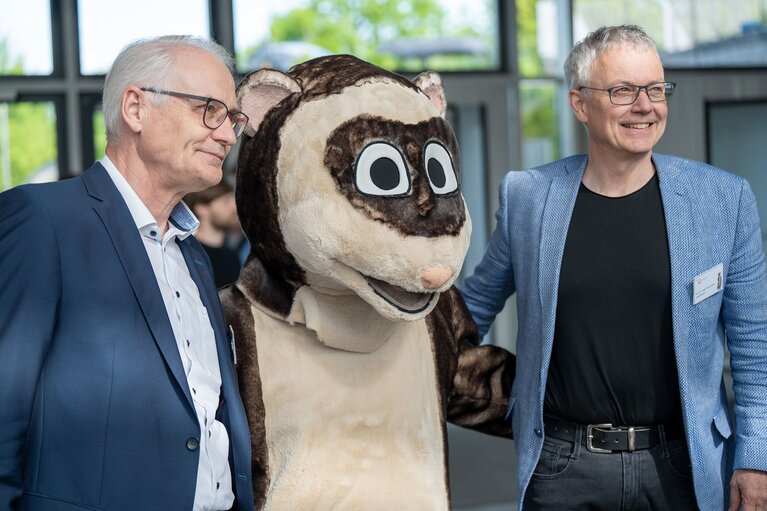 Zwei Männer und ein Maskottchen in der Mitte