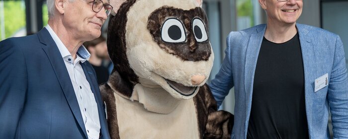 Zwei Männer und ein Maskottchen in der Mitte
