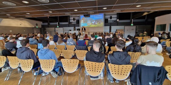 Studierende im Hörsaal von hinten bei der Begrüßung durch den Präsidenten auf der Bühne