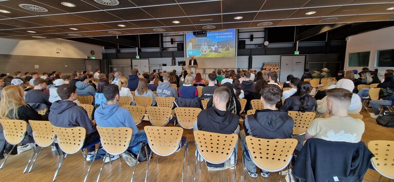 Studierende im Hörsaal von hinten bei der Begrüßung durch den Präsidenten auf der Bühne