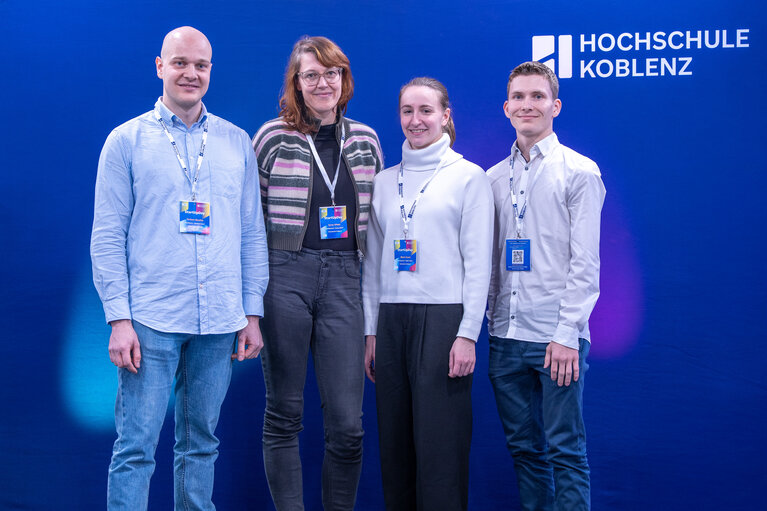 Vier Personen vor einer blauen Wand mit Logo der Hochschule Koblenz.
