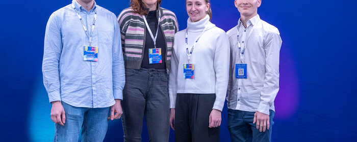 Vier Personen vor einer blauen Wand mit Logo der Hochschule Koblenz.