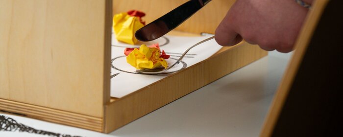 Eine Hand versucht mit Messer und Gabel.