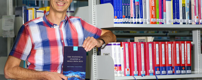 Professor Neuhäuser mit seinem Buch in der Bibliothek der Hochschule.
