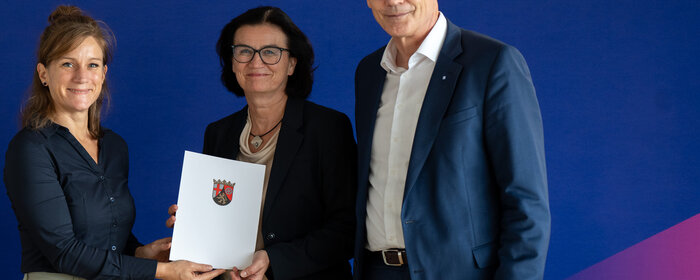 Zwei Frauen und ein Mann stehen zusammen und halten eine Mappe mit dem Förderbescheid in der Hand.