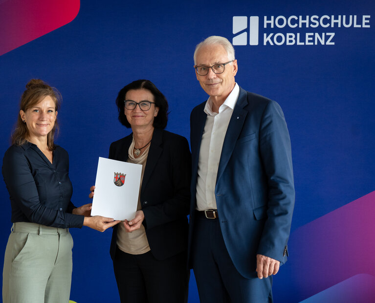 Zwei Frauen und ein Mann stehen zusammen und halten eine Mappe mit dem Förderbescheid in der Hand.