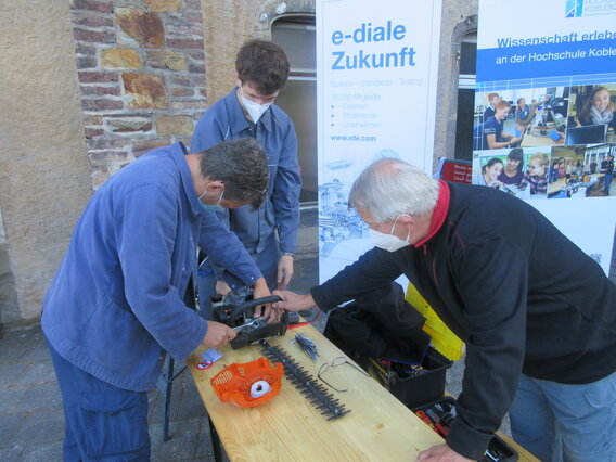 Drei Männer reparieren eine elektrische Heckenschere