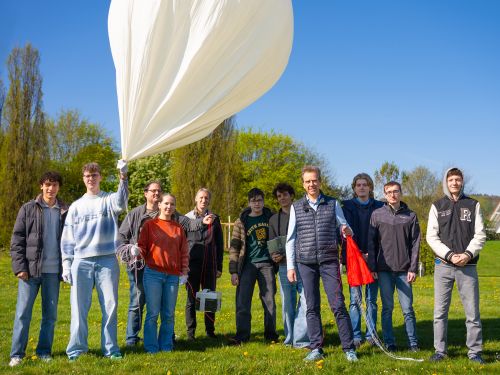 Die Teilnehmenden stehen auf einer Wiese und halten den Ballon, die Nutzlastsonde sowie den Fallschrim in der Hand.